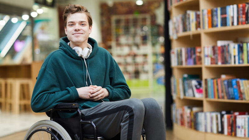Étudiant en fauteuil roulant portant un casque autour du cou dans une bibliothèque
