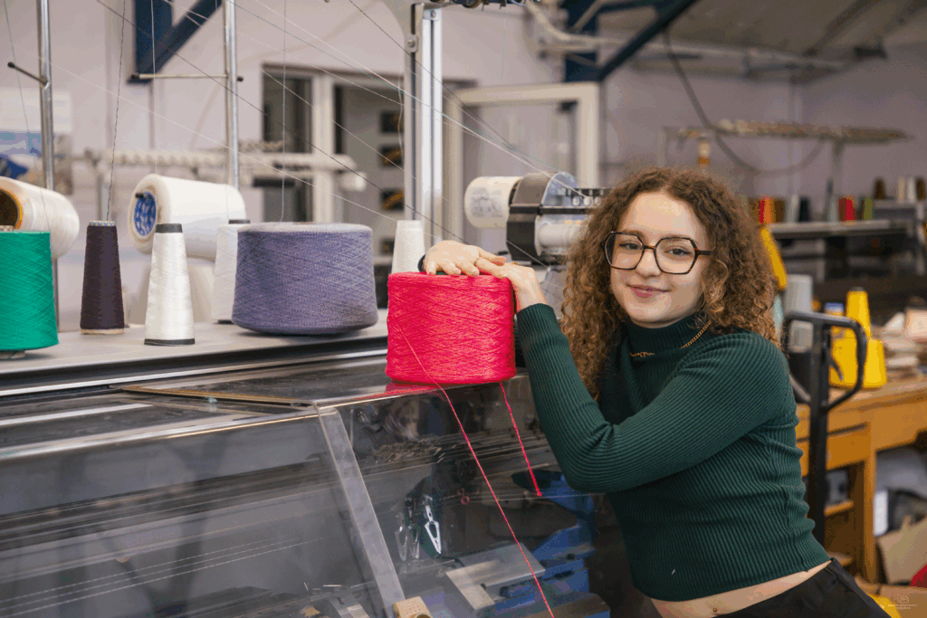 Etudiante devant une machine textile avec une bobine à la main